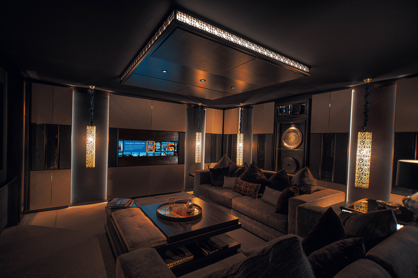 A dark cinema room with a large screen, lounge seating and concealed equipment