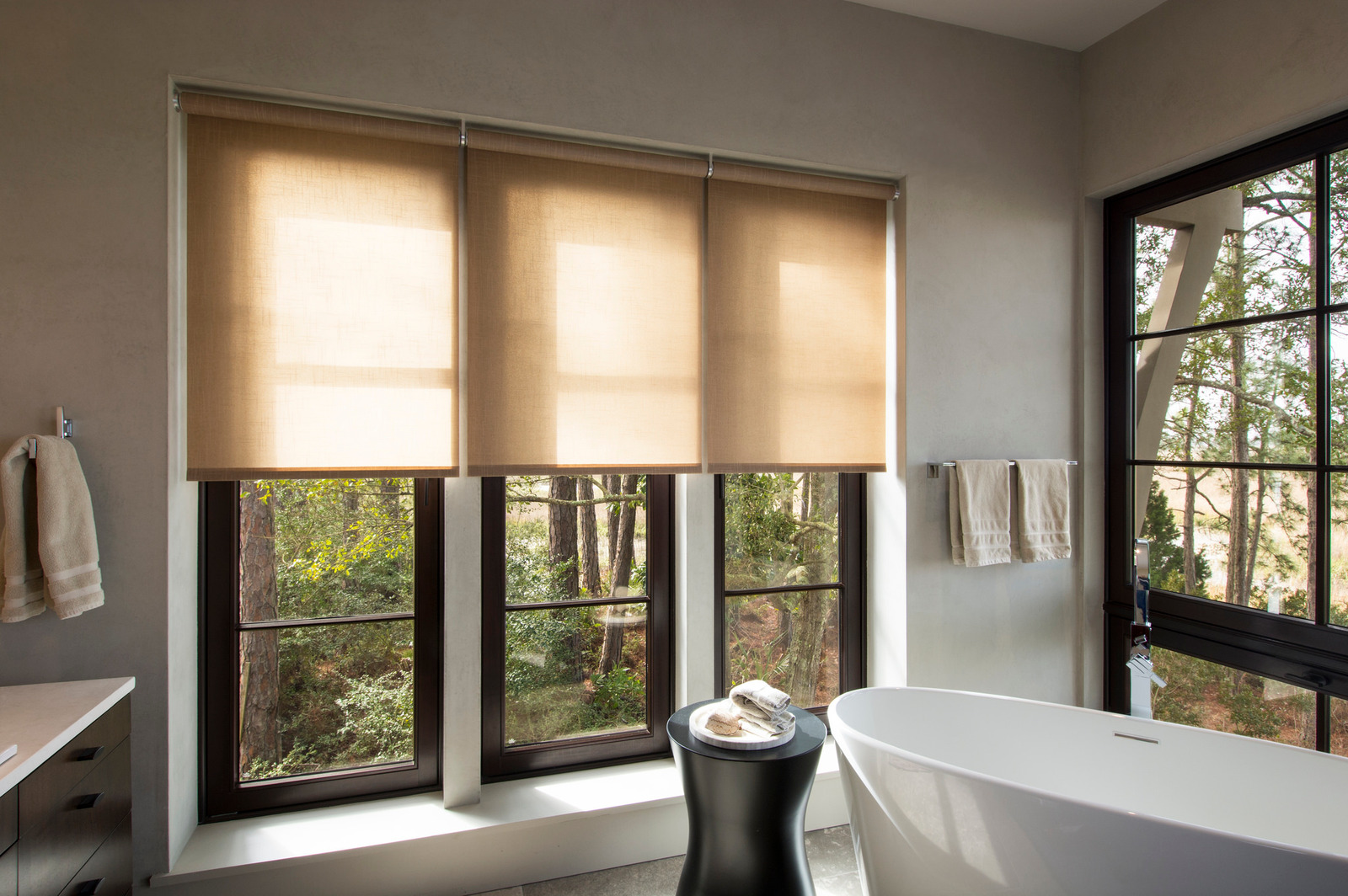 Roller shades softening daylight above a freestanding bathtub