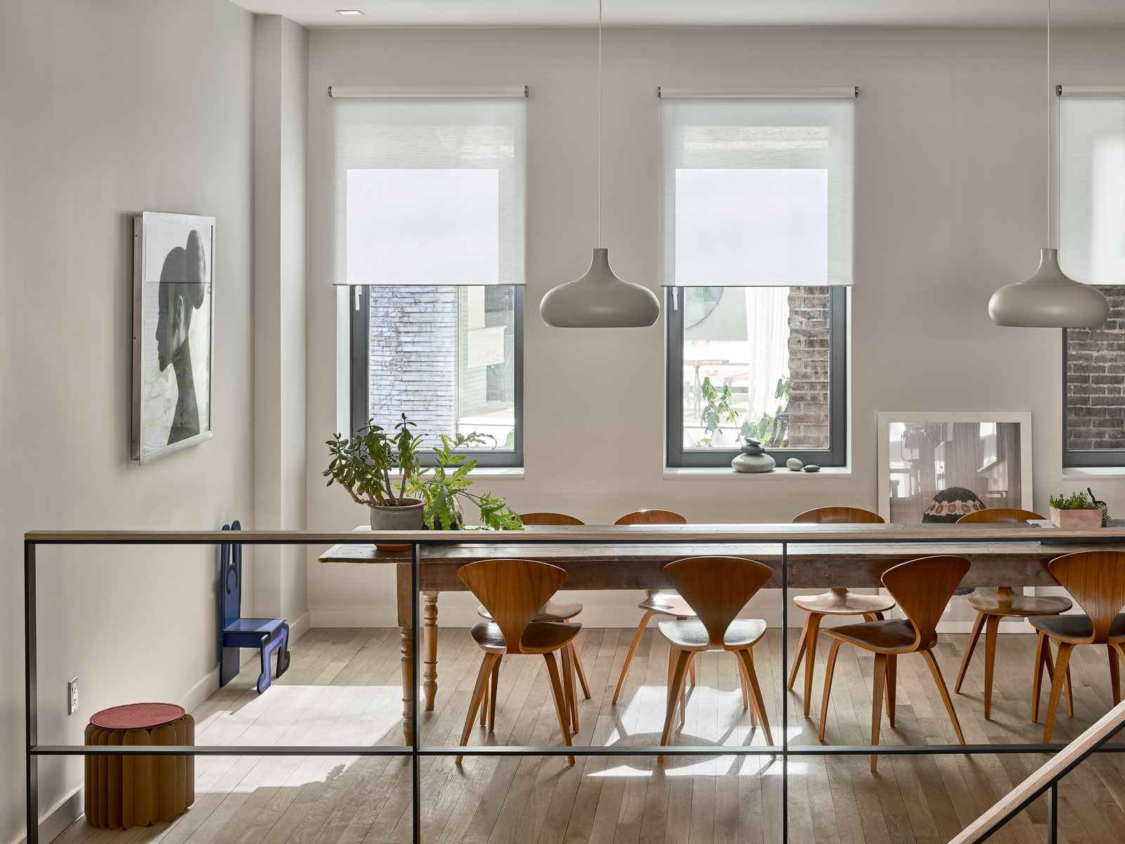 A daylit loft dining area with timber chairs, pendant lights and roller shades