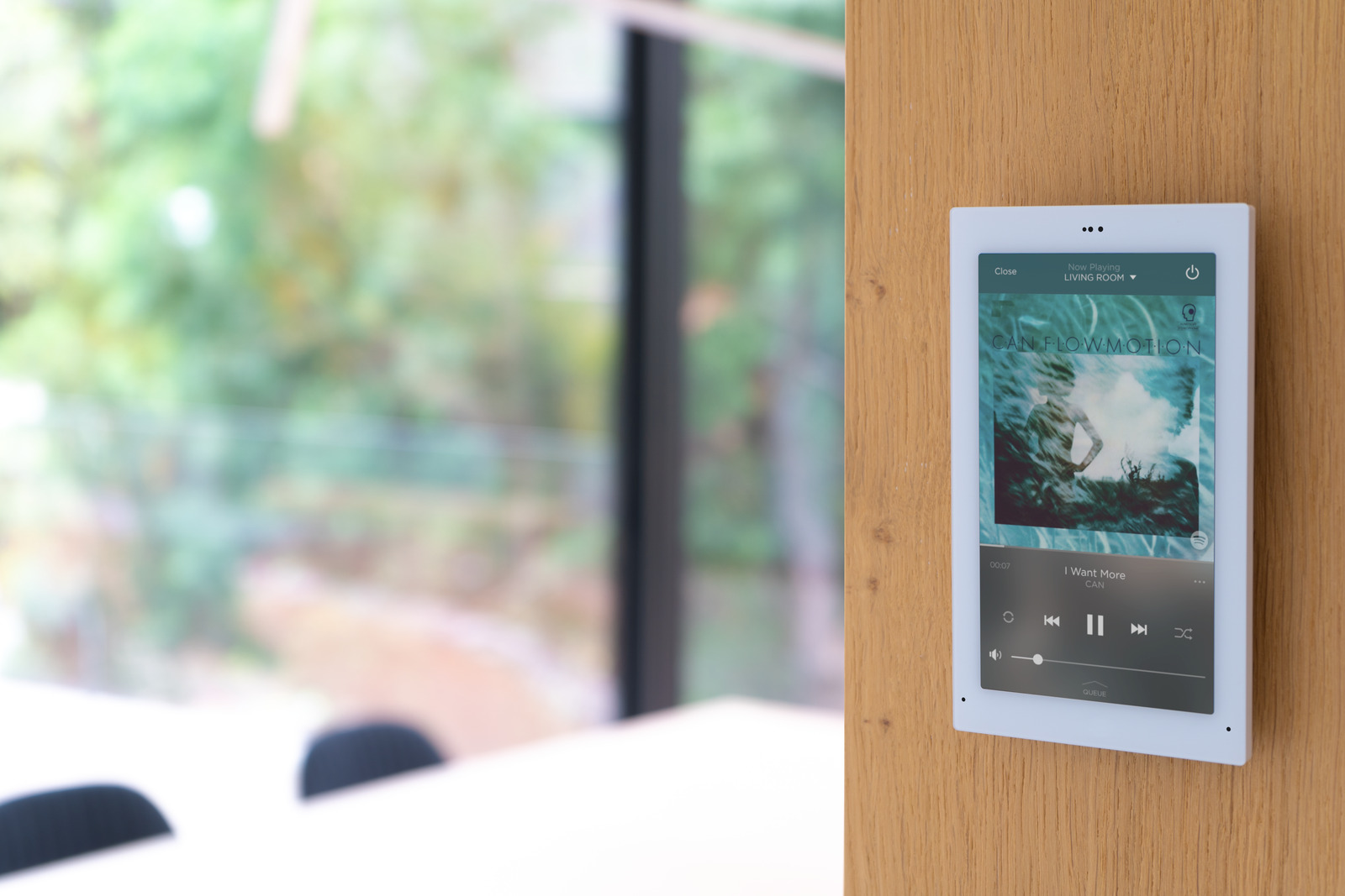 A Savant wall touchscreen displaying a Now Playing music interface beside a window
