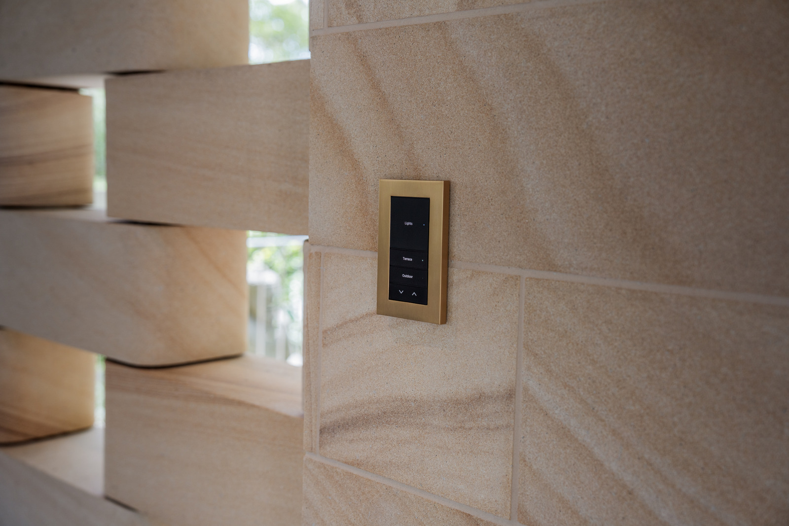 A dark Control4 Lux keypad on a stone wall beside a curved staircase
