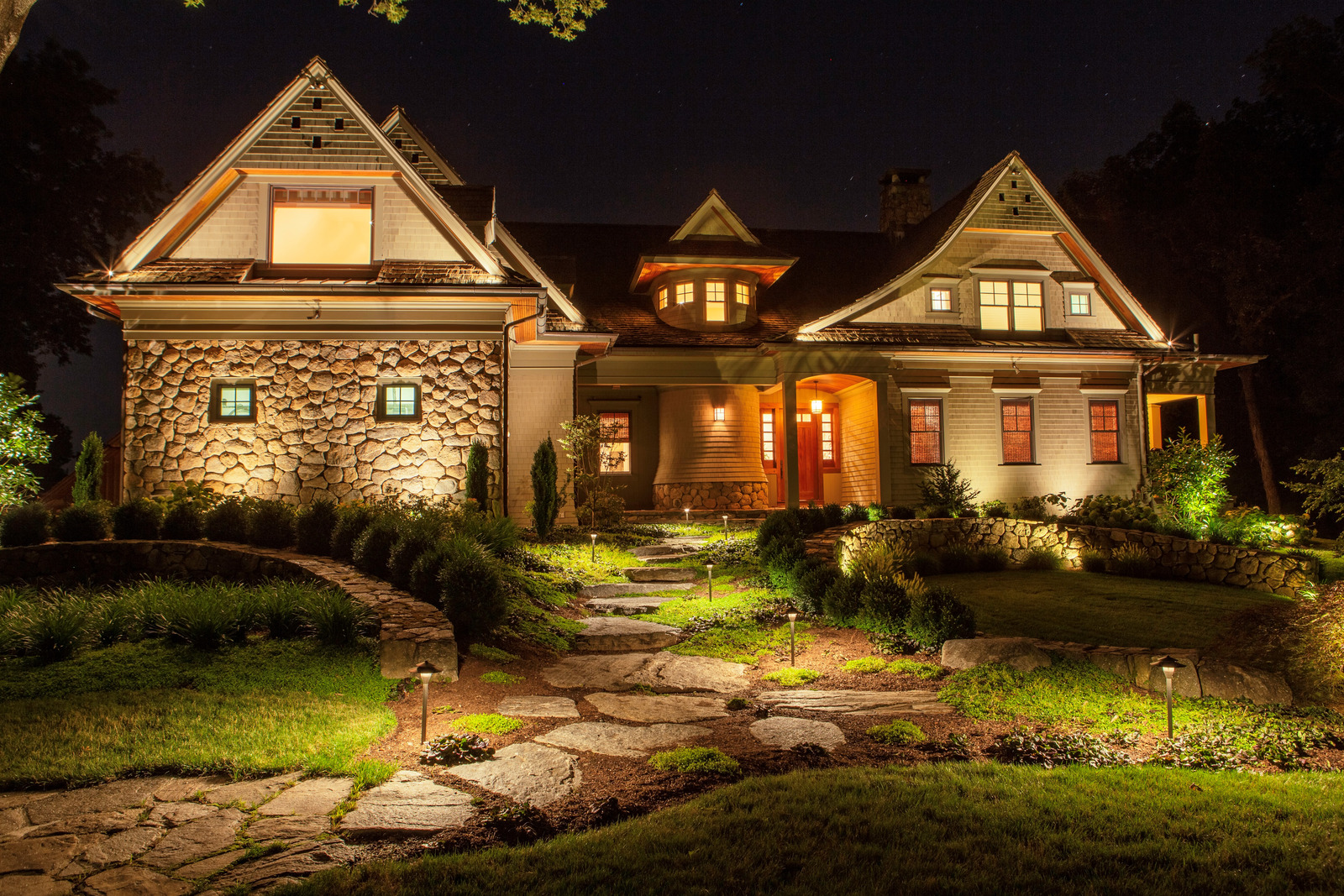 Warm landscape lighting illuminates a stone path, planting and the front of a home at night