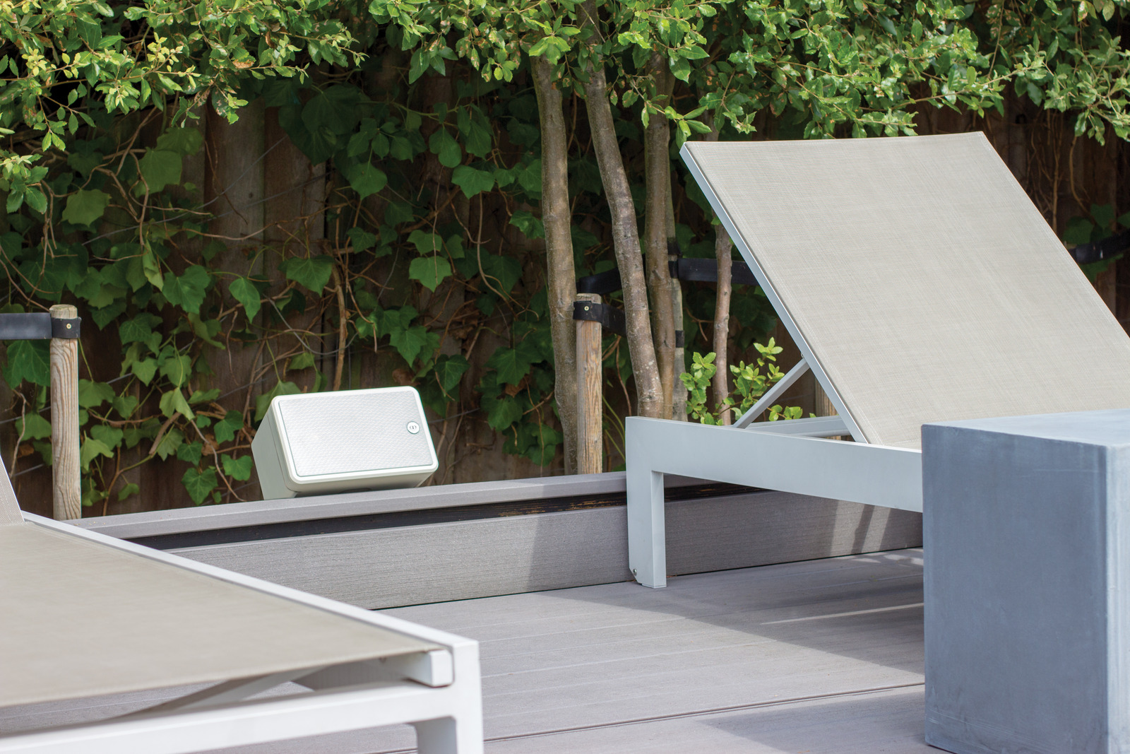 A white Monitor Audio speaker mounted beside poolside loungers